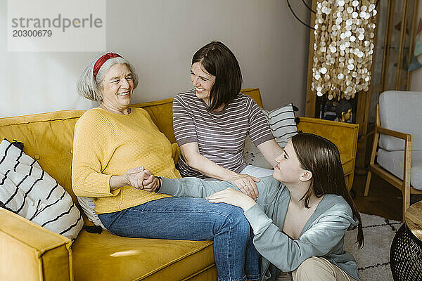 Glückliche Seniorin verbringt ihre Freizeit mit Enkelin und Schwiegertochter  während sie zu Hause auf dem Sofa sitzt