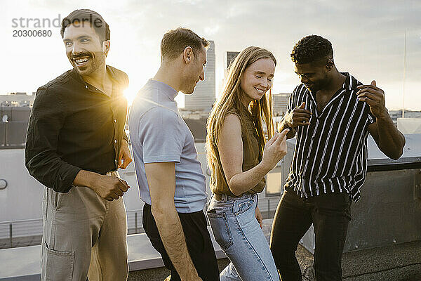 Fröhliche männliche und weibliche gemischtrassige Freunde tanzen bei Sonnenuntergang auf der Terrasse