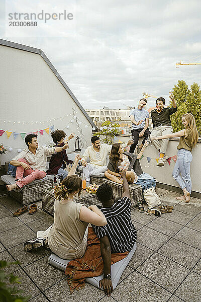 Glückliche männliche und weibliche gemischtrassige Freunde  die während der Party auf der Dachterrasse Getränke anstoßen