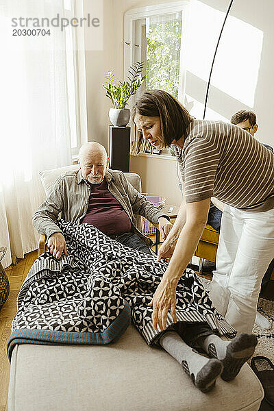 Frau kümmert sich um den älteren Schwiegervater  während sie zu Hause auf einem Stuhl sitzt