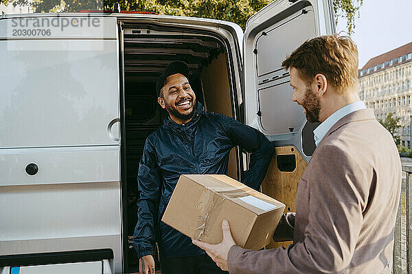 Reifer Mann erhält Paket von männlichem Zusteller  der in der Nähe des Kofferraums eines Lieferwagens steht