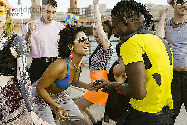 Glückliche nicht-binäre Person  die Sonnenbrille trägt und mit Freunden in der Stadt tanzt