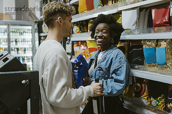 Lächelnde junge Frau kauft mit ihrem Freund ein  während sie am Gang im Supermarkt steht