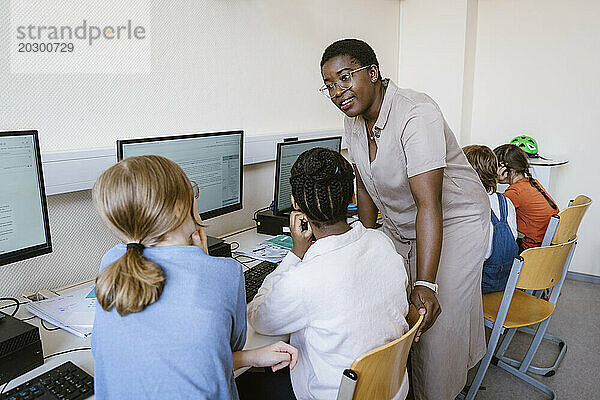 Lehrerin spricht mit Kindern  die in der Computerklasse in der Schule sitzen