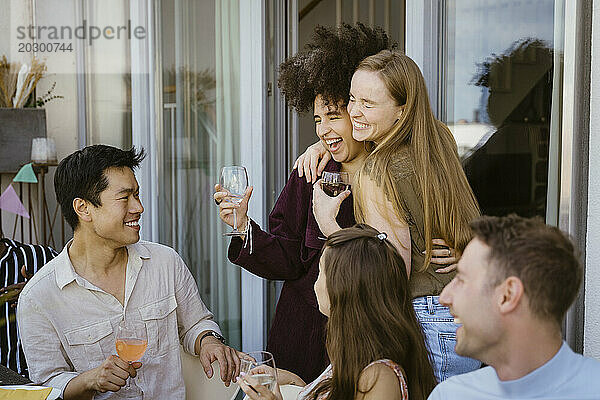 Fröhliche Frau umarmt ihre Freundin und genießt Getränke  während sie auf dem Balkon eine Dinnerparty feiert