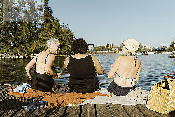 Rückansicht älterer Freundinnen  die Spaß haben  während sie auf einem Hausboot in der Nähe des Sees sitzen