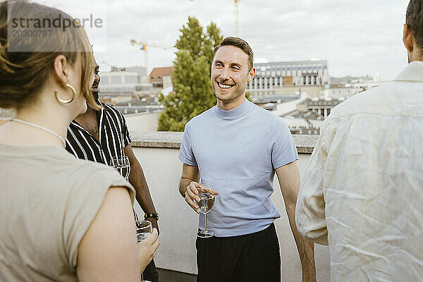 Fröhliche männliche und weibliche Freunde genießen Getränke auf der Party auf dem Balkon