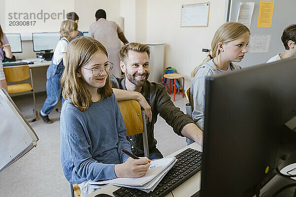 Lächelnder männlicher Lehrer mit Schülern  die im Computerunterricht in der Schule lernen