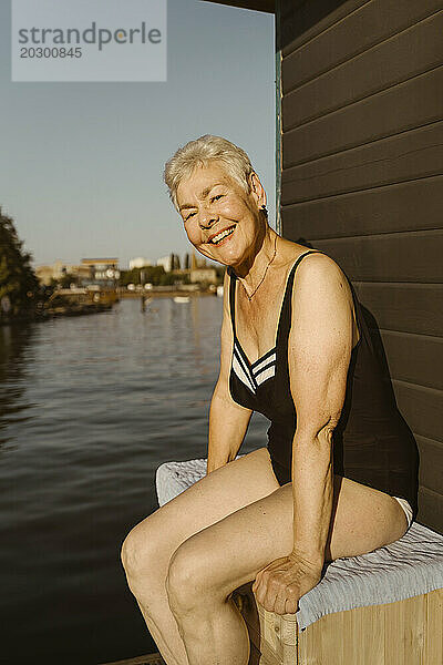 Porträt einer glücklichen Seniorin im Badeanzug  während sie auf einem Hausboot am See sitzt