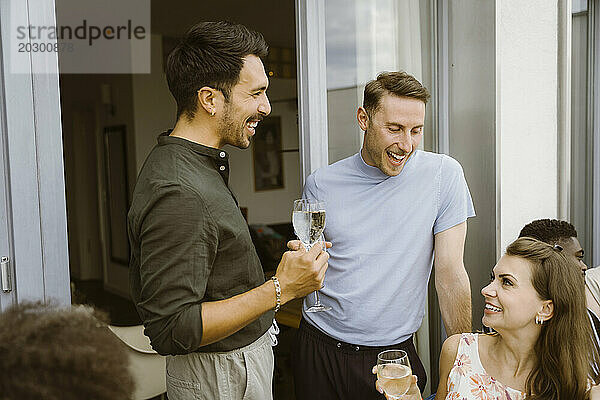 Fröhliche männliche Freunde genießen Drinks mit einer Freundin bei einer Dinnerparty auf dem Balkon