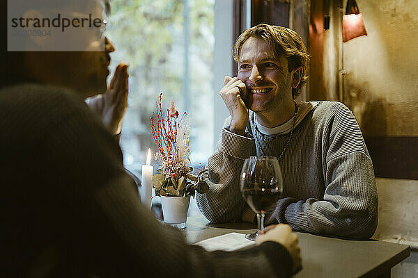 Glücklicher schwuler Mann  der mit seinem Freund während eines Candle-Light-Date im Restaurant spricht