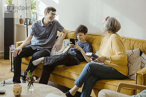 Glücklicher Mann sitzt mit Sohn und Schwiegermutter zu Hause auf dem Sofa