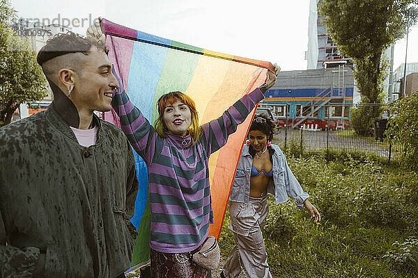 Frau hält LGBT-Flagge in der Hand  während sie mit nicht-binären Freunden im Park spazieren geht