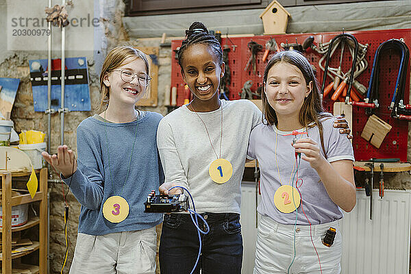 Porträt glücklicher Studentinnen  die während eines Technologie-Workshops in der Schule elektrische Teile zeigen