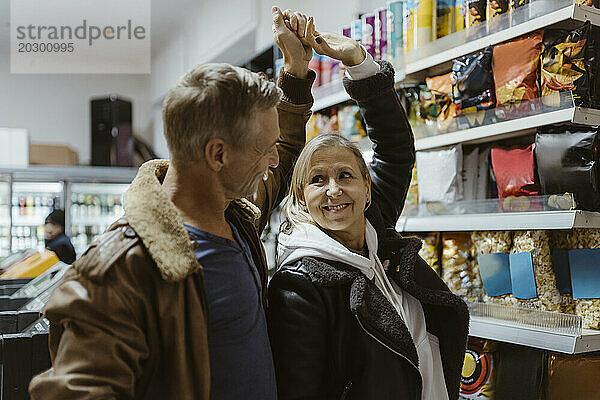 Glückliches älteres Paar tanzt zusammen mit erhobener Hand beim Einkaufen im Supermarkt