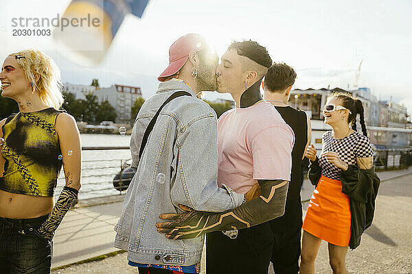 Zärtlicher schwuler Mann küsst nicht-binäre Person auf der Promenade in der Stadt
