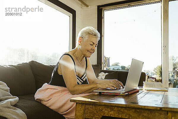 Ältere Frau benutzt Laptop  während sie auf dem Sofa im Hausboot sitzt
