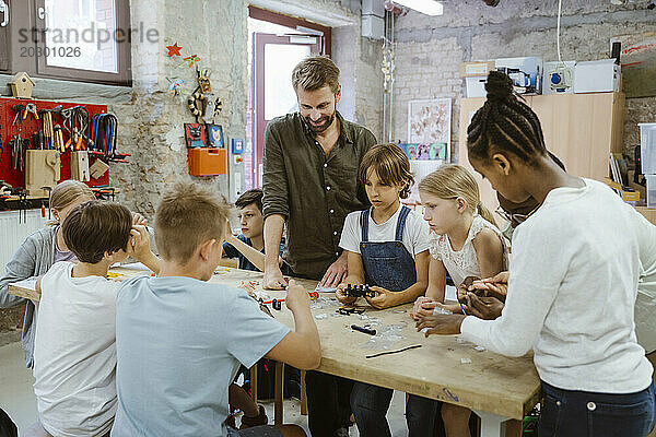 Männlicher Lehrer mit einer Gruppe von Schülern  die in der Technologiewerkstatt in der Schule an einem Robotikprojekt arbeiten