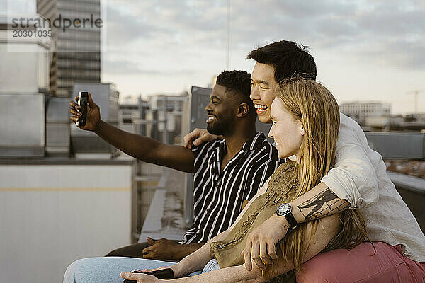 Junger Mann macht ein Selfie mit Freunden per Smartphone  während er auf der Terrasse sitzt