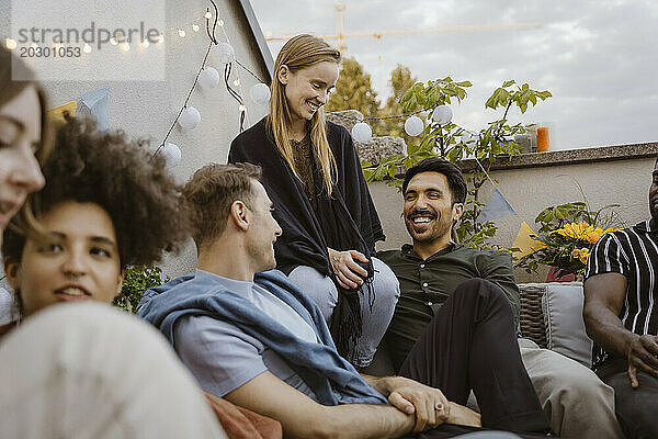 Gruppe männlicher und weiblicher Freunde unterhält sich  während sie auf einer Party auf dem Balkon sitzt