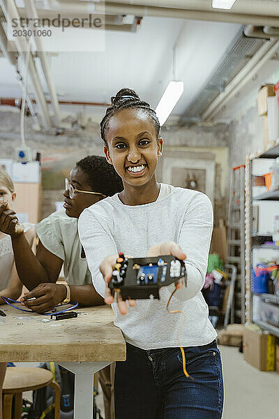 Porträt eines lächelnden Mädchens  das elektrische Komponenten in der Technologiewerkstatt der Schule zeigt