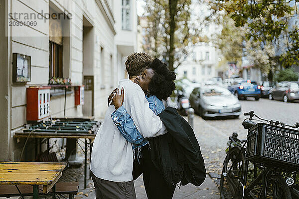 Seitenansicht eines Mannes  der seine gemischtrassige Freundin umarmt  während er auf dem Bürgersteig in der Stadt steht