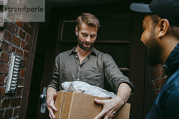 Reifer Mann erhält Paket von Kurierzusteller  während er vor der Haustür steht