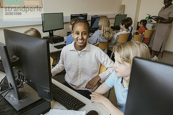 Porträt eines lächelnden Mädchens  das mit Freunden im Computerklassenzimmer der Schule auf einem Stuhl sitzt