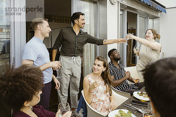 Lächelnde Frau reicht einem männlichen Freund bei einer Dinnerparty auf dem Balkon ein Weinglas