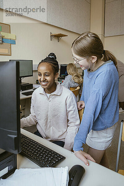 Glückliche  gemischtrassige Mädchen  die Spaß im Computerunterricht in der Schule haben
