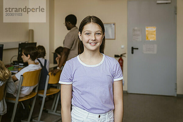 Porträt eines lächelnden Mädchens  das in der Computerklasse in der Schule steht