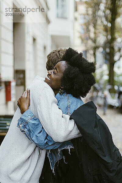 Seitenansicht einer glücklichen Frau  die ihren Freund mit dem Arm umarmt  während sie auf dem Bürgersteig in der Stadt steht