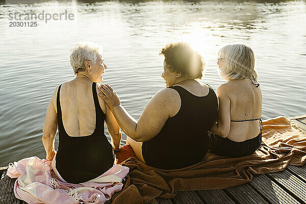 Glückliche ältere Freundinnen unterhalten sich  während sie im Urlaub auf einem Hausboot in der Nähe des Sees sitzen