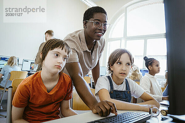 Lächelnde Lehrerin unterstützt Mädchen mit Down-Syndrom im Computerunterricht in der Schule