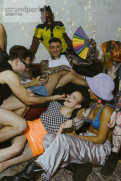 Nicht-binäre Person lacht  während sie sich während einer Party in der Wohnung inmitten von Freunden hinlegt