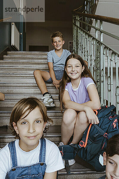 Porträt männlicher und weiblicher Schüler  die auf einer Treppe sitzen