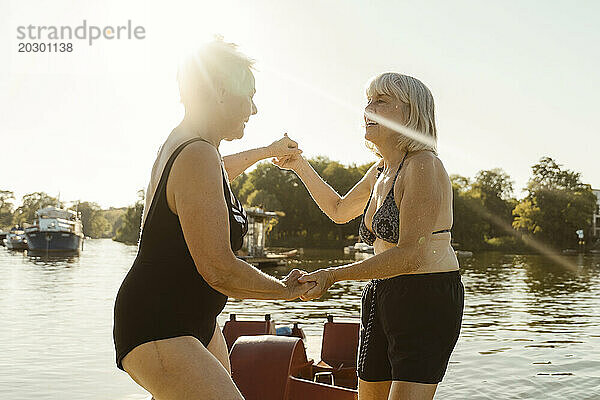 Fröhliche ältere Freundinnen halten sich im Urlaub an den Händen und tanzen auf dem Hausboot