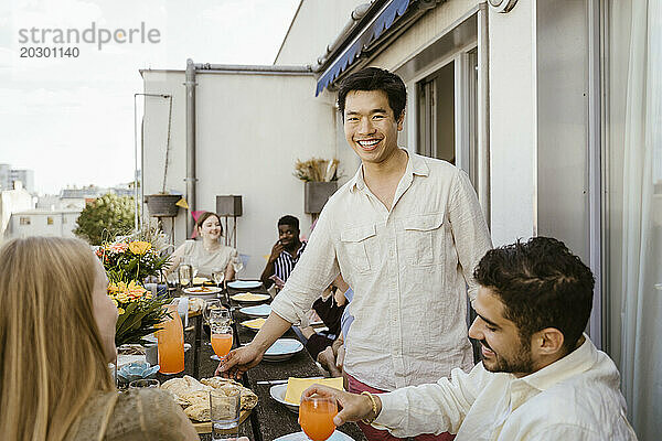 Porträt eines lächelnden Mannes mit männlichen und weiblichen Freunden  die eine Dinnerparty auf dem Balkon genießen