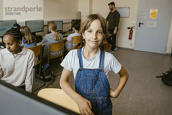 Porträt eines lächelnden Mädchens  das mit der Hand auf der Hüfte im Computerklassenzimmer im Büro steht