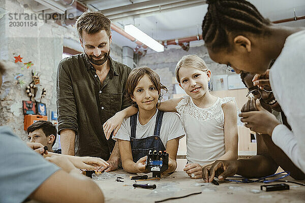 Porträt eines lächelnden Mädchens mit dem Arm um eine Freundin inmitten von Lehrern und Schülern in der Technologiewerkstatt in der Schule
