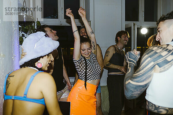 Lächelnde nicht-binäre Person  die mit erhobenen Armen inmitten von Freunden im Nachtclub tanzt