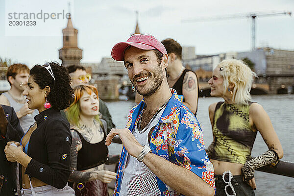 Porträt eines lächelnden schwulen Mannes mit Blumenmuster  der mit nicht-binären Freunden in der Stadt tanzt