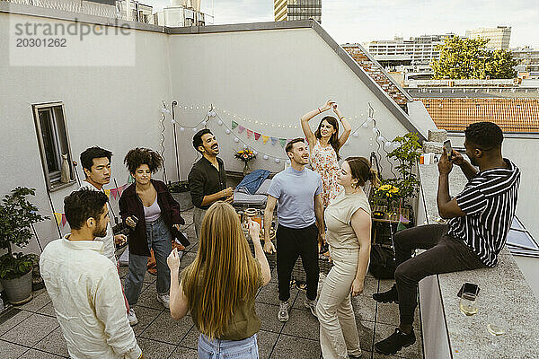 Junger Mann fotografiert männliche und weibliche Freunde  die auf einer Party auf der Dachterrasse tanzen