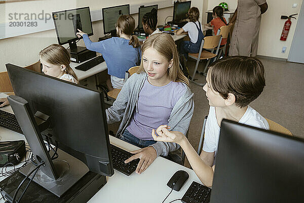 Blick aus der Vogelperspektive auf männliche und weibliche Klassenkameraden  die diskutieren  während sie in der Computerklasse in der Schule sitzen