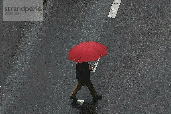 Eine Person in Schöneberg läuft mit einem Regenschirm über die Straße in Berlin  22.03.2024