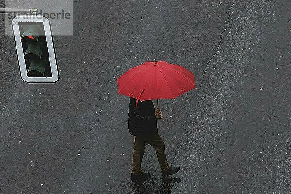 Eine Person in Schöneberg läuft mit einem Regenschirm über die Straße in Berlin  22.03.2024