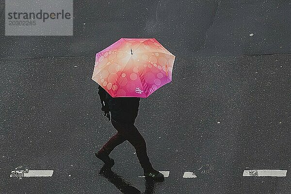 Eine Person in Schöneberg läuft mit einem Regenschirm über die Straße in Berlin  22.03.2024