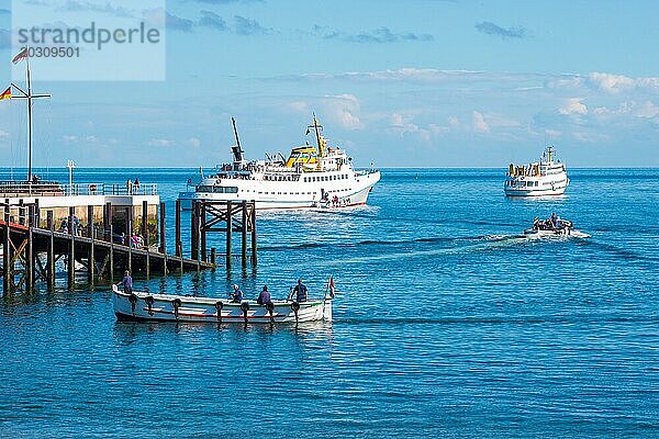 Zwei weiße Fähren  'Fair Lady' und 'Lady von Büsum'  Einschiffen  Einbooten vor der Insel Helgoland  2 Börteboote  traditionelles Börteboot  Boote mit Menschen auf offenem Meer unter blauem Himmel  ruhiges  blaues Wasser  Holzpier  sonniger Tag  Schleswig-Holstein  Deutschland  Europa