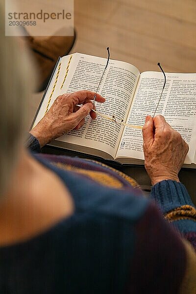 Eine ältere Person sitzt und liest in einem Buch  die Brille in den Händen haltend  Bibelkreis  Jesus Grace Chruch  Ludwigsburg  Deutschland  Europa