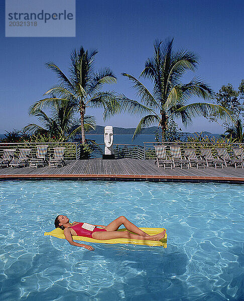 Australien. Queensland. Lindeman Island Resort. Junge Frau entspannt sich auf einer Lilo im Schwimmbad.